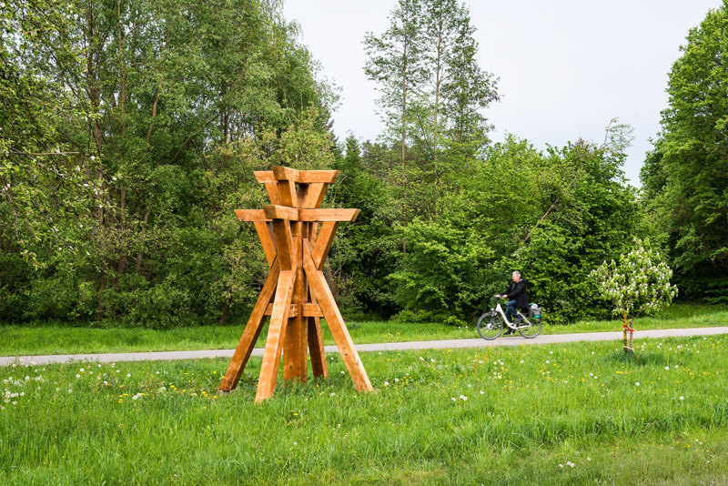 Holzskulptur mit Radfahrer im Hintergrund